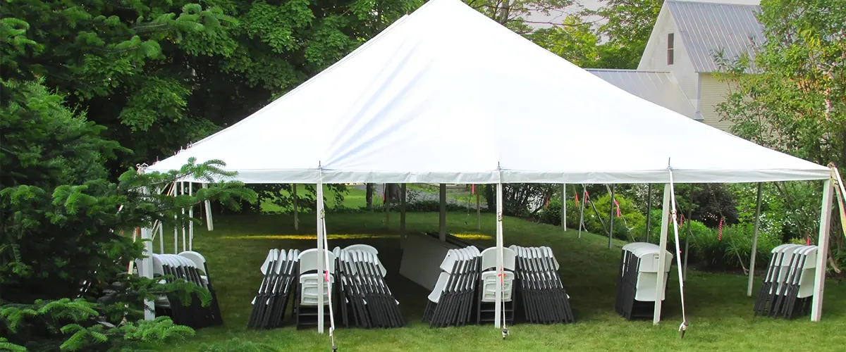 A canopy tent on a lawn with plastic chairs and tables