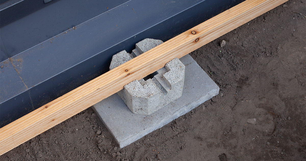 A concrete deck block with a piece of lumber and a metal frame