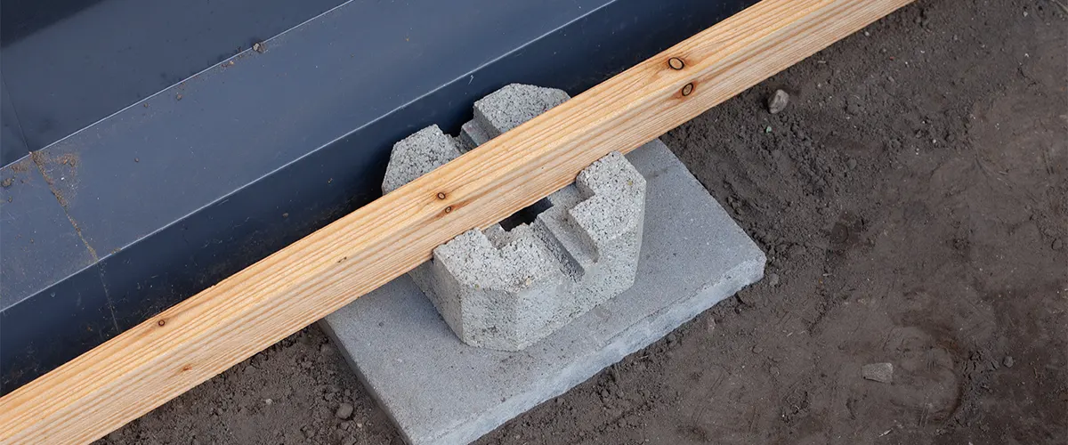 A concrete deck block with a piece of lumber and a metal frame