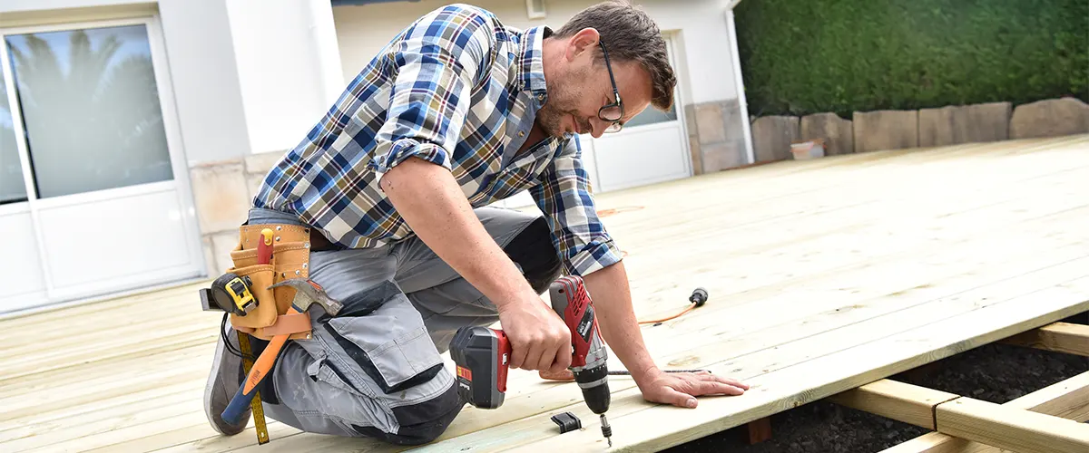 A deck builder installing decking boards with a power drill