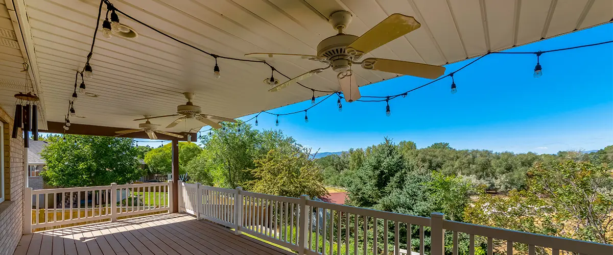 under deck ceiling with wood flooring and white railings under the ceiling fans and string lights.