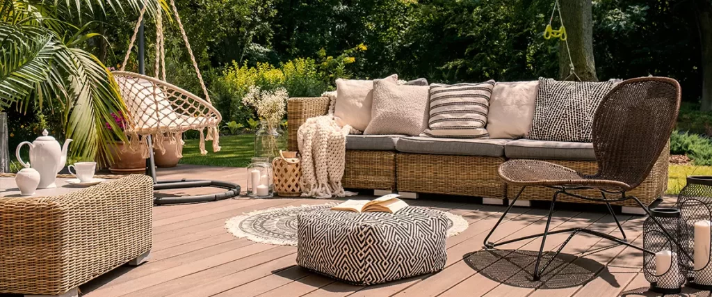 A rattan patio set including a sofa, a table and a chair on a wooden deck in the sunny garden.