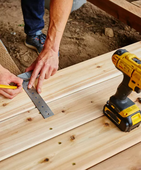 man drilling and measuring wood for deck Deck Installation Cost In Oak Ridge TN
