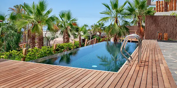 Luxurious swimming pool with clear blue water and surrounded by tropical palm trees and redwood decking