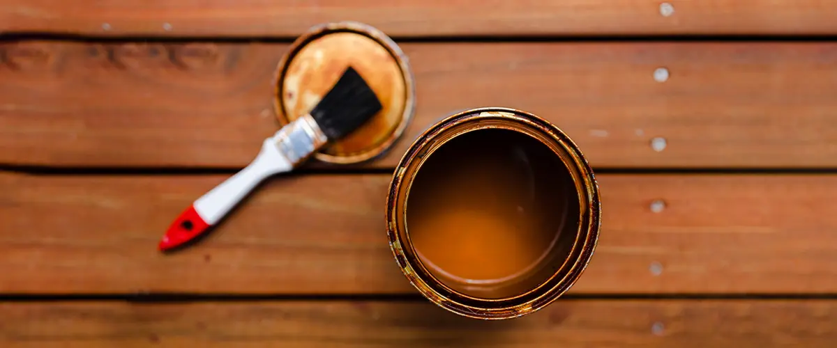 Open can of Best Deck Paint For Old Wood with brush on aged planks.