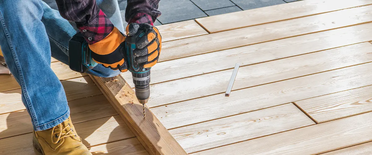 Carpenter using cordless drill on wooden deck during construction.