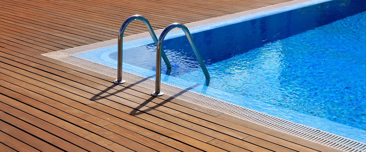 Close-up of blue swimming pool with stainless steel ladder and wooden deck.