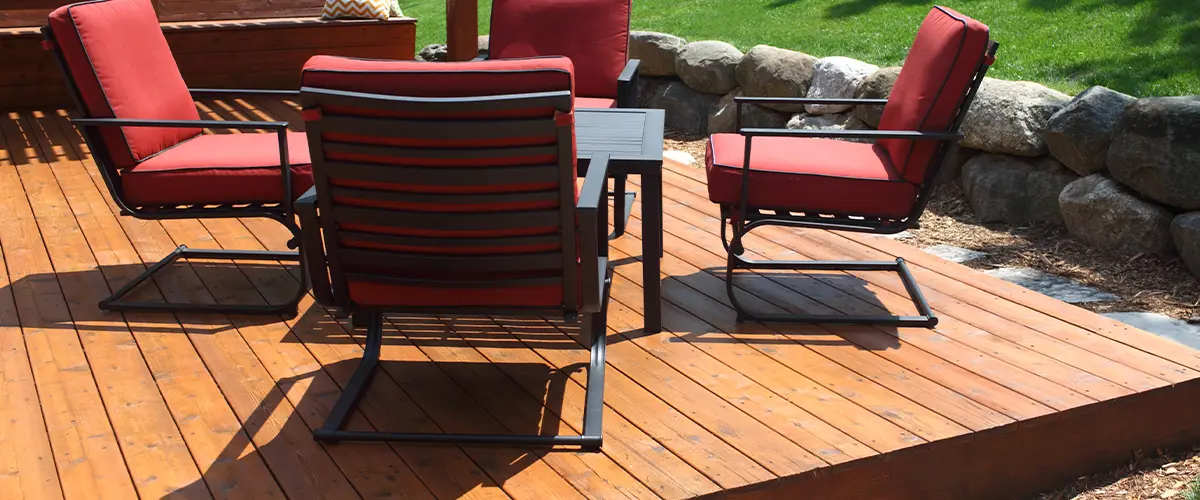 Outdoor wooden deck with red patio furniture and green lawn background. Deck Fascia Installation in Knoxville, TN