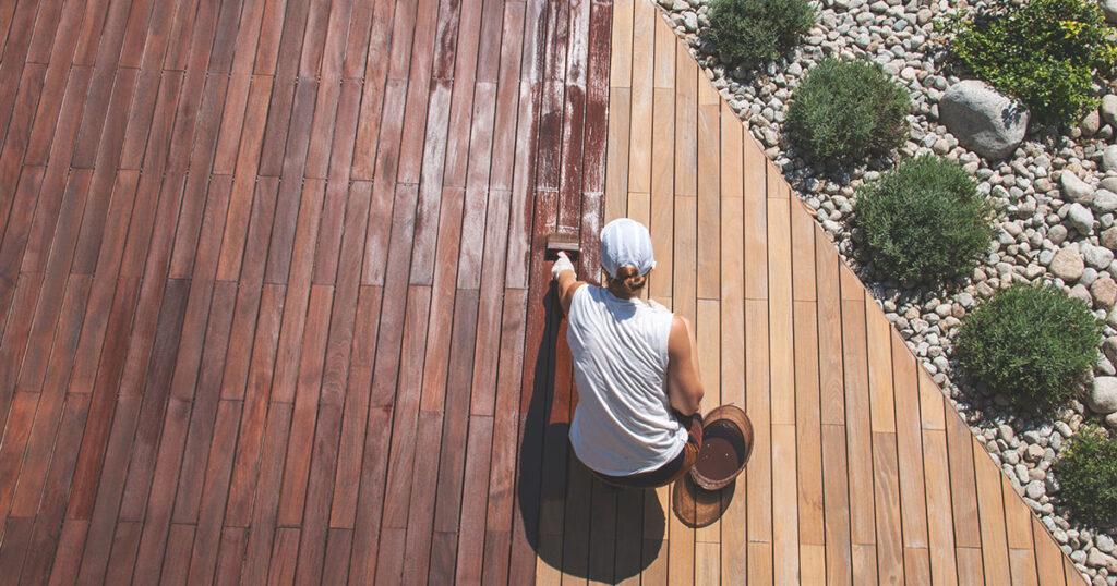 Wood deck renovation treatment, the person applying protective wood stain with a brush, overhead view of ipe hardwood decking restoration process