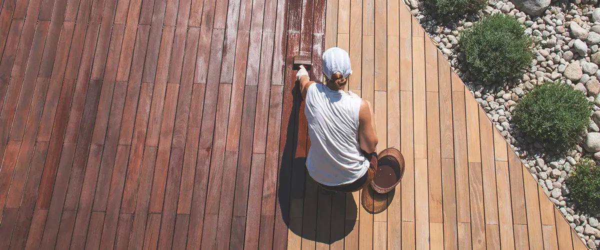 Wood deck renovation treatment, the person applying protective wood stain with a brush, overhead view of ipe hardwood decking restoration process