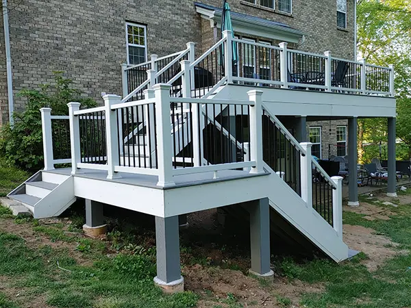 Modern raised deck with white railings and black balusters, featuring multiple levels, stairs, and outdoor seating area against a brick house. Riverview decks project