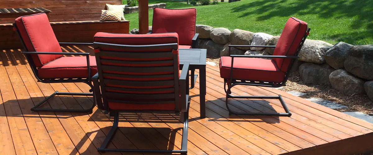 Wooden deck in Amherst, Knoxville, with red cushioned chairs and a table, surrounded by green grass and trees, creating a cozy outdoor seating area.