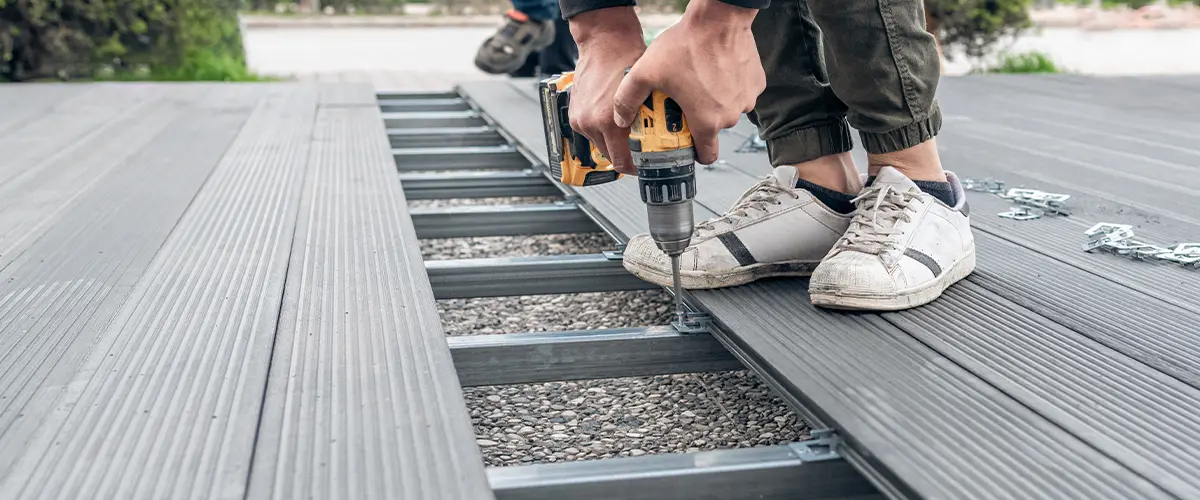 Worker drilling screws into a grey composite deck, wearing casual clothes and sneakers, focused on precise alignment, for deck replacement in Amherst, Knoxville