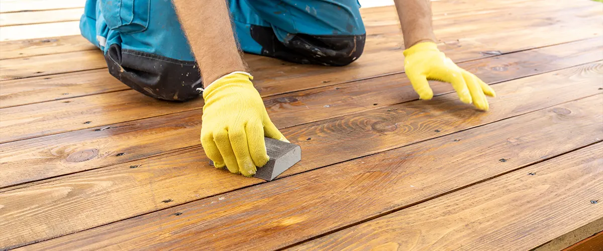 Close-up of worker hand-sanding a wooden deck during a refinishing project - deck restoration and maintenance service.