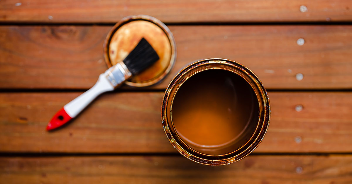 Open can of wood stain with a paintbrush on a wooden deck - preparation for deck staining and refinishing project.