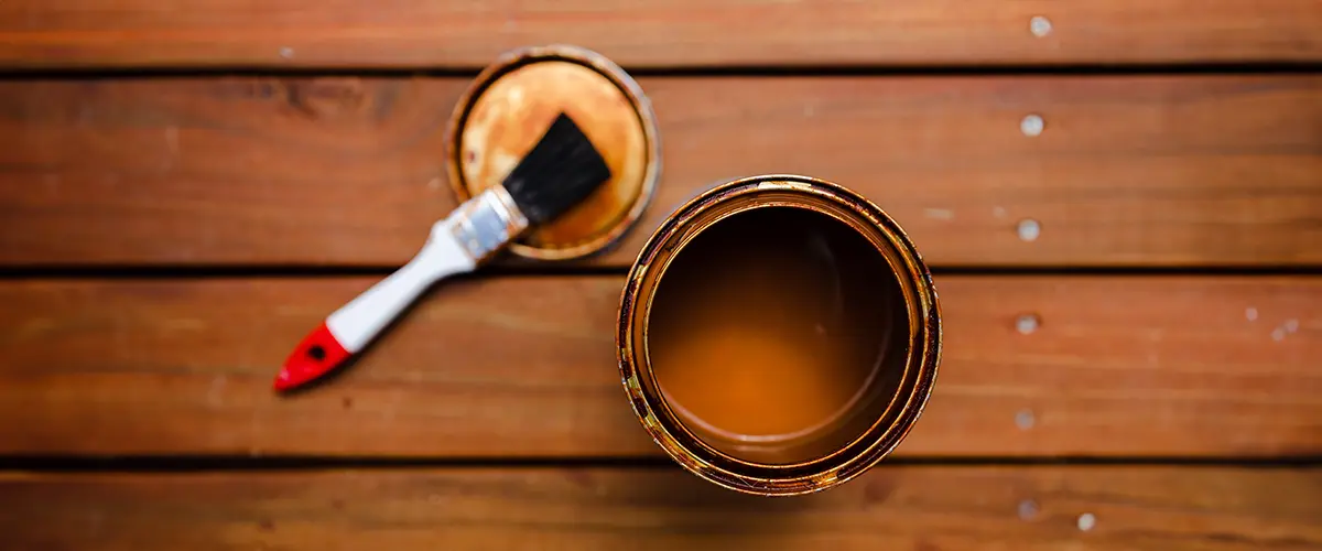 Open can of wood stain with a paintbrush on a wooden deck - preparation for deck staining and refinishing project.