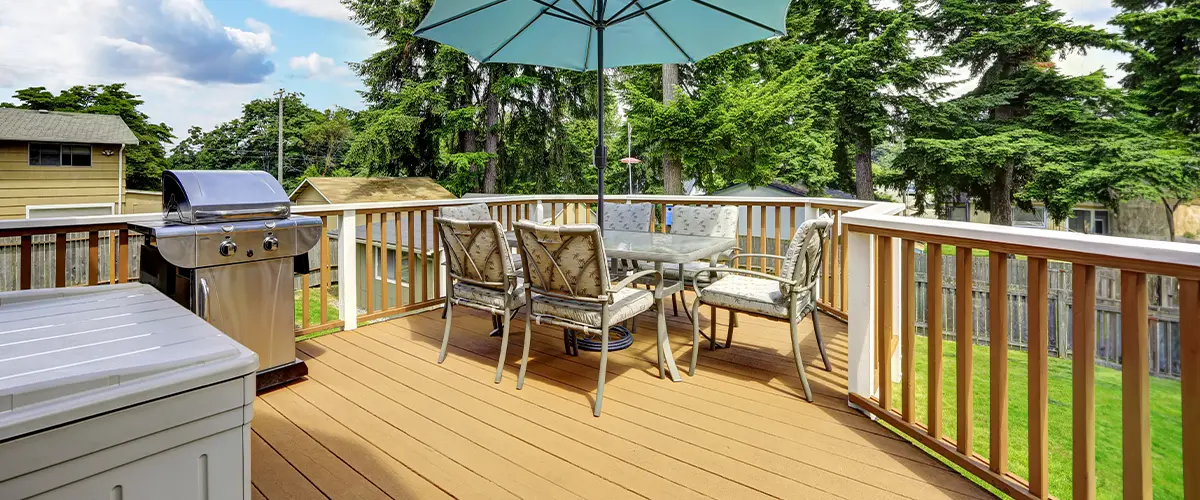 Outdoor deck installation in Seymour, with patio furniture, a BBQ grill, and a blue umbrella, surrounded by a green backyard with tall trees.