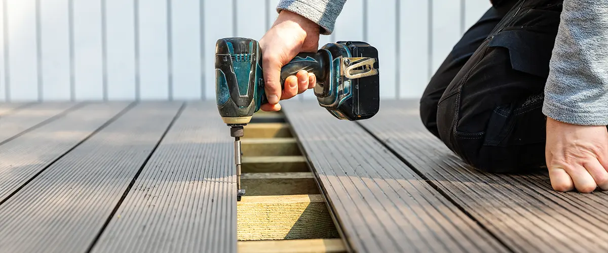 Person using a power drill to install composite decking boards on a wooden frame, in seymour, focusing on detailed craftsmanship.