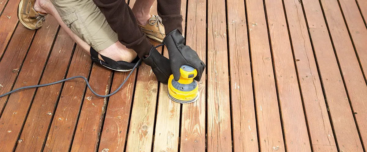 Worker sanding a wooden deck with an electric sander during a deck refinishing project - deck maintenance and restoration.