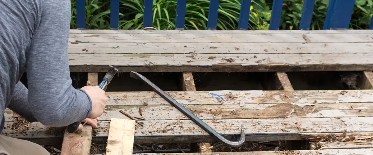 Person replacing old wooden deck boards with crowbar and hammer