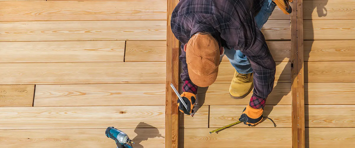 Construction worker measuring wood planks while building a new outdoor deck, emphasizing precision and craftsmanship.