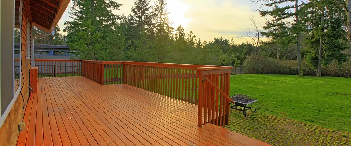 Spacious wood deck overlooking a lush backyard with sunset view, perfect for outdoor relaxation.