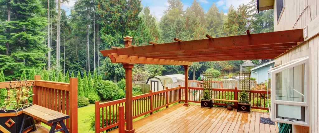 A spacious wooden deck with a pergola, wooden railing, and a lush green backyard