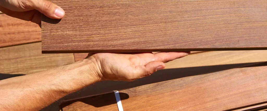 Person holding a wooden deck board over a stack of similar boards