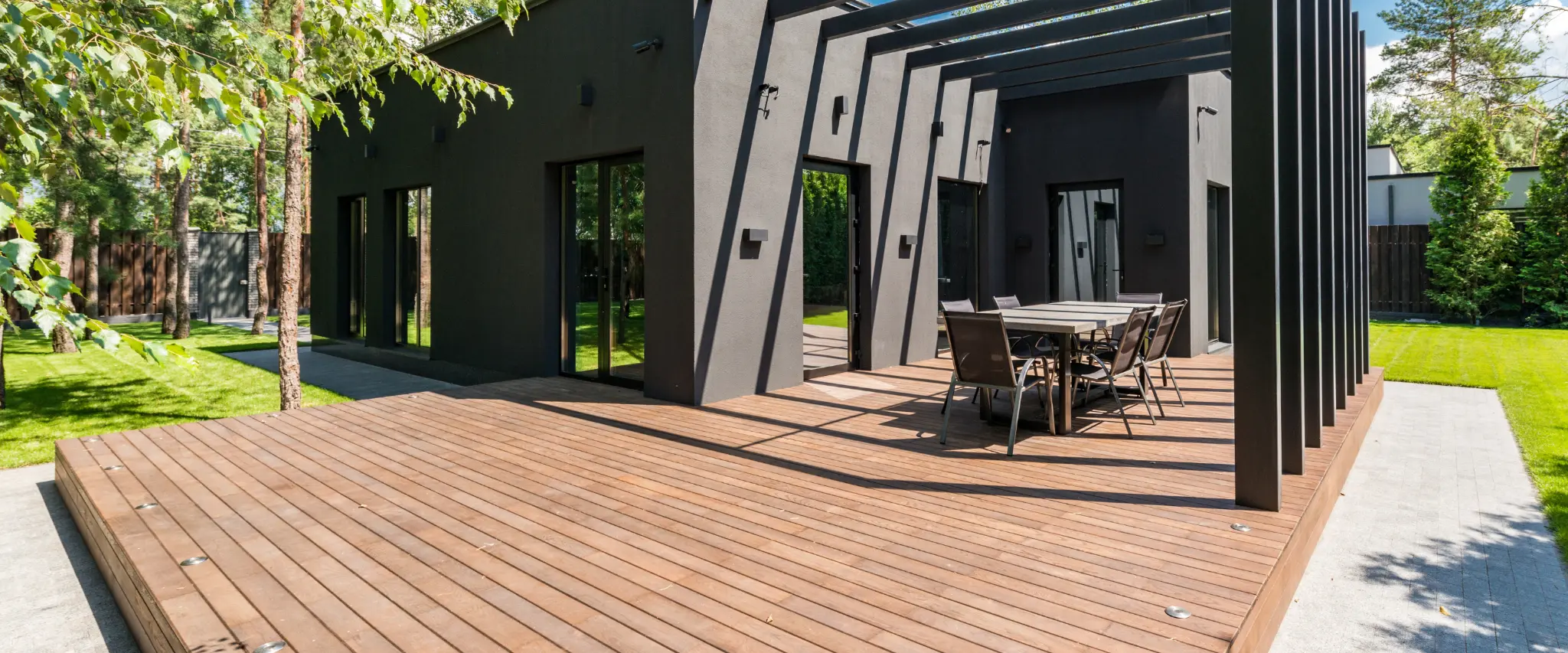 Modern outdoor deck with pergola, surrounded by lush greenery