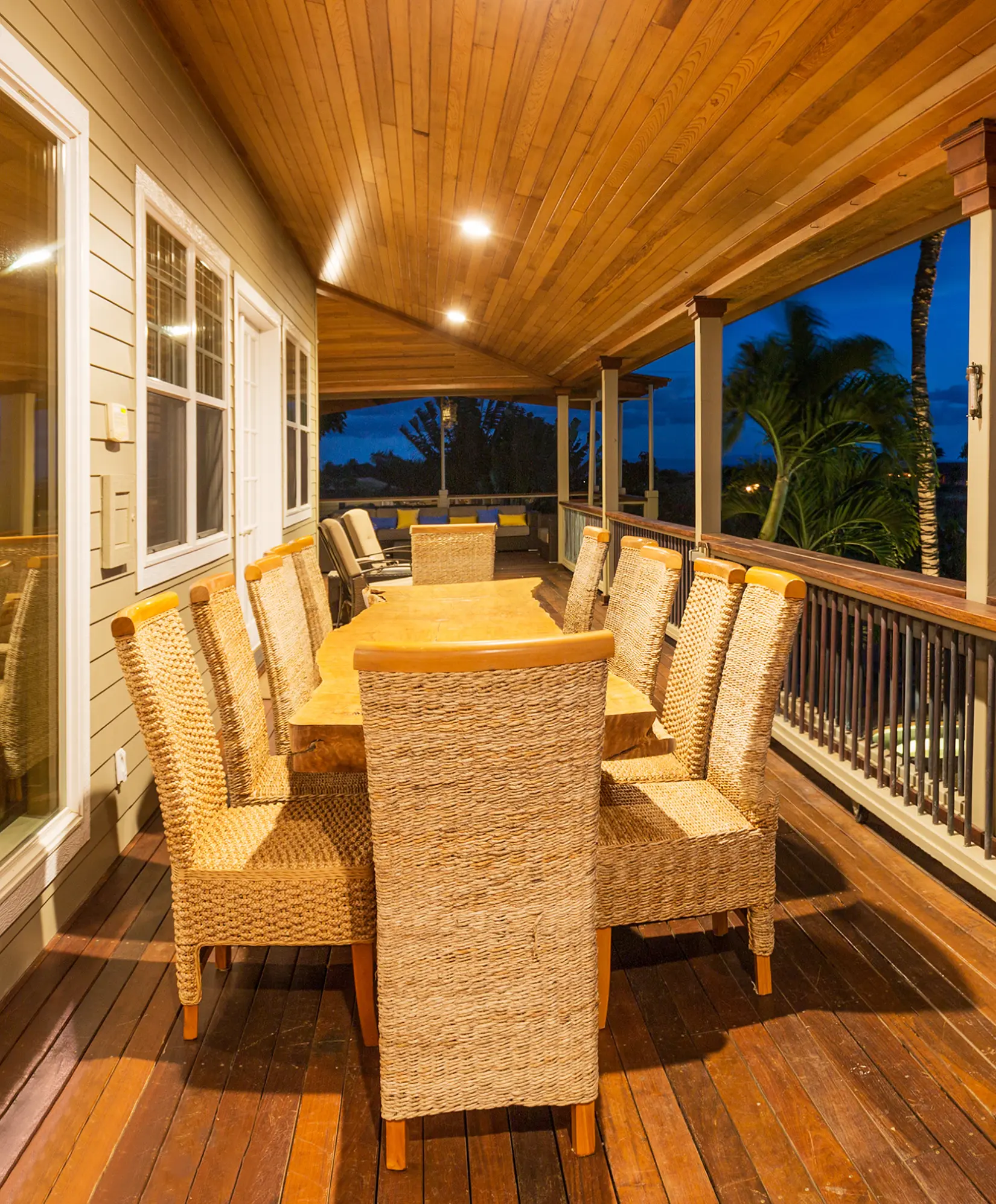 Elegant covered deck with a long dining table and woven chairs at night.