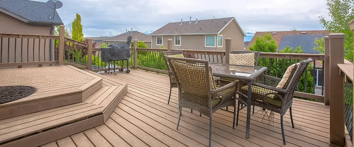 Backyard composite deck with patio dining set and BBQ grill, featuring custom railings and step-down platform.