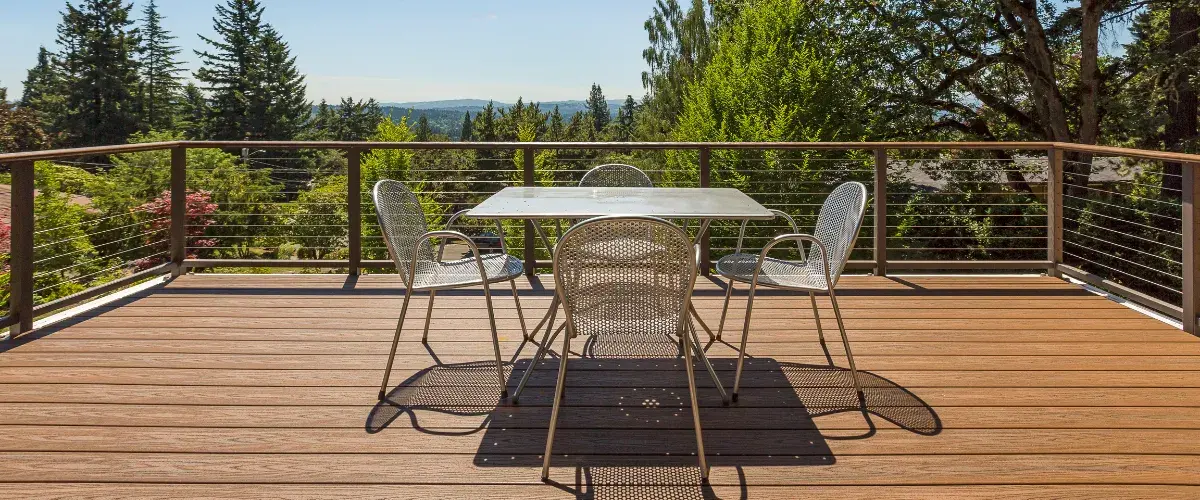 Elevated wood deck with metal cable railing and outdoor dining set offering scenic views of lush trees and mountains