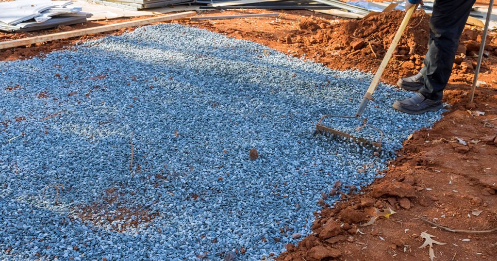 Worker spreading gravel base layer for backyard deck foundation and drainage support during construction
