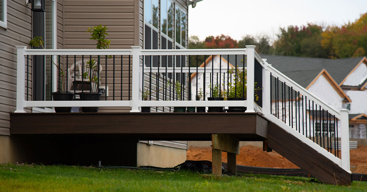 Raised backyard deck with stairs, white railing, and potted plants attached to a modern house