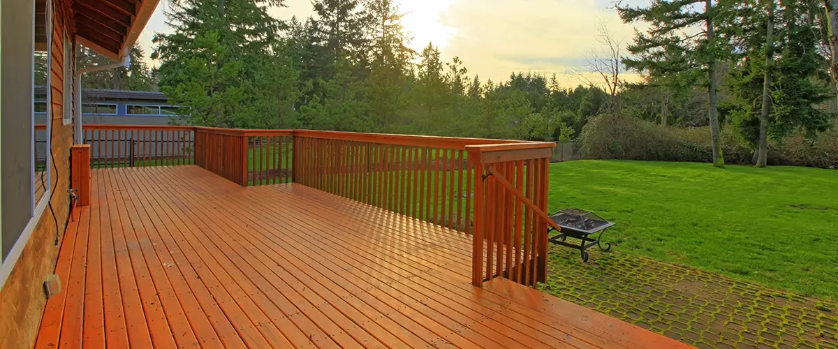 Spacious wooden backyard deck with railing surrounded by green lawn and trees perfect for outdoor living