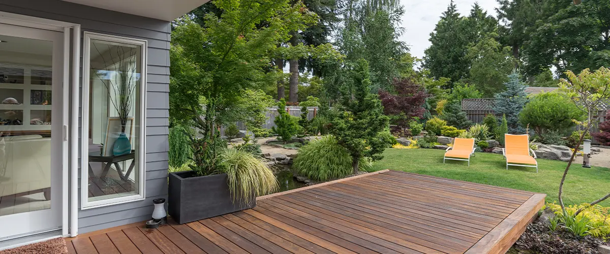 Modern backyard wood deck with koi pond, lush landscaping, and bright orange patio loungers for relaxation.