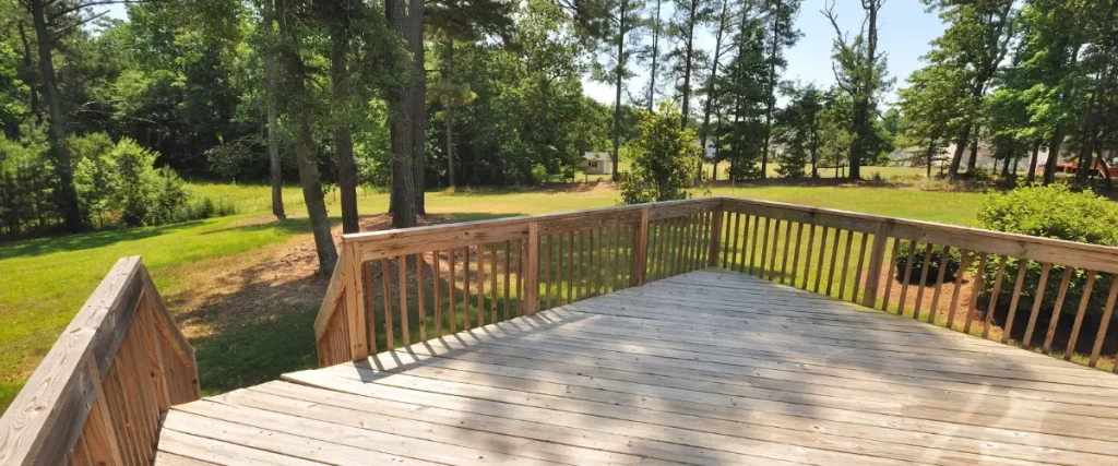 Spacious backyard wood deck with railing surrounded by trees and grass