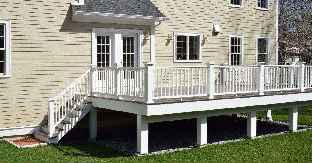 Elevated composite deck with white railings on a beige house