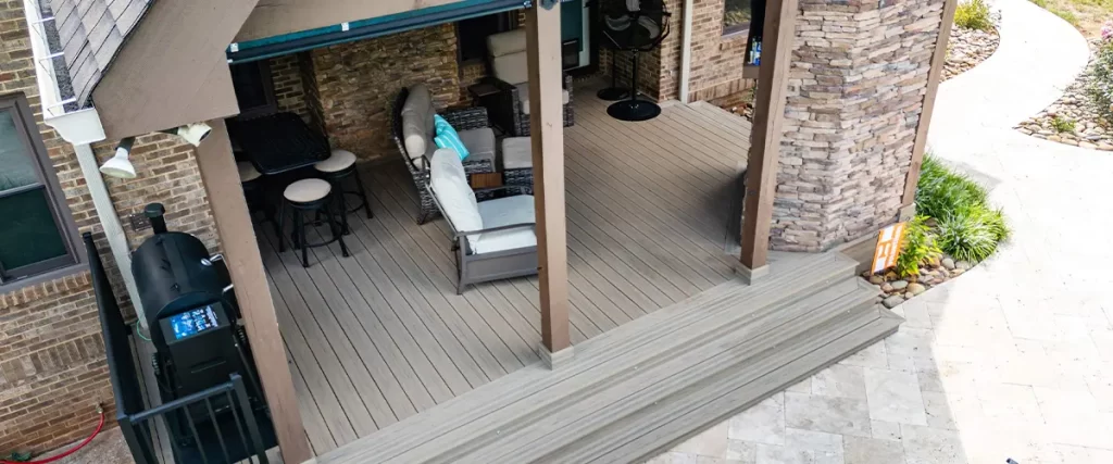 Covered composite deck with outdoor seating and grill area, featuring stone columns and wood beams.