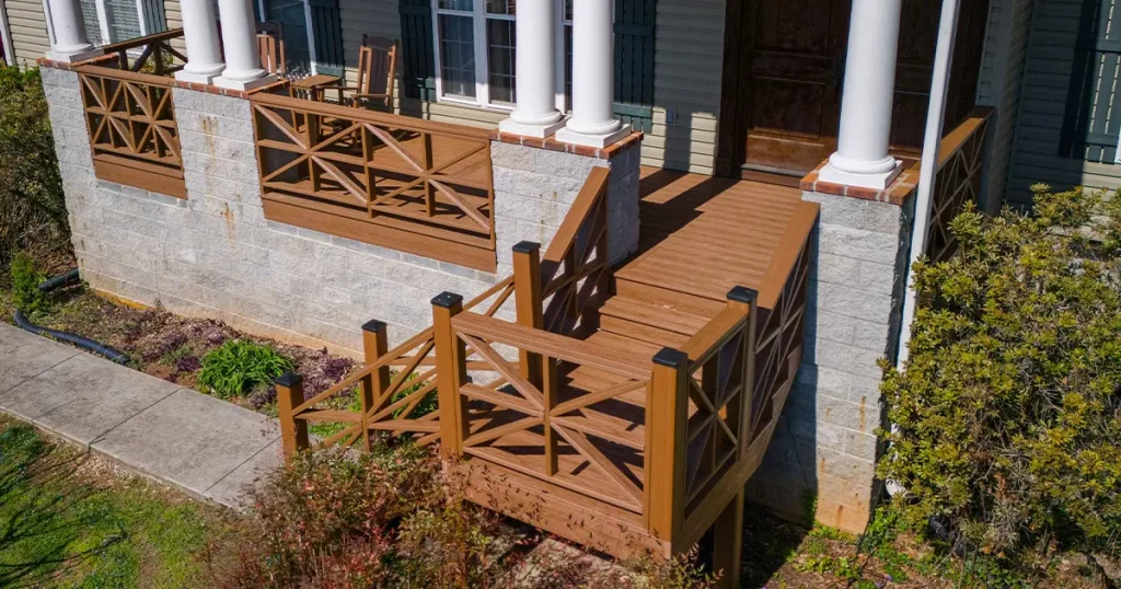 Elevated front porch with composite decking, decorative railing, and column supports on stone foundation - featured