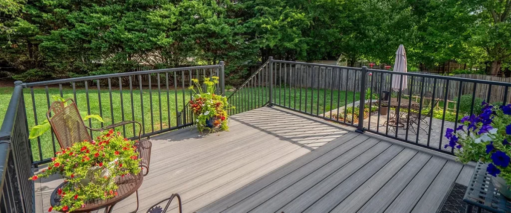 Gray composite deck with black railing and garden view, connected to lower patio with dining area.