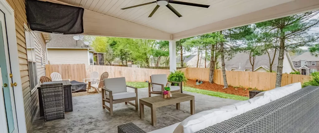Spacious stamped concrete patio with white ceiling, black fan, and wicker outdoor furniture.