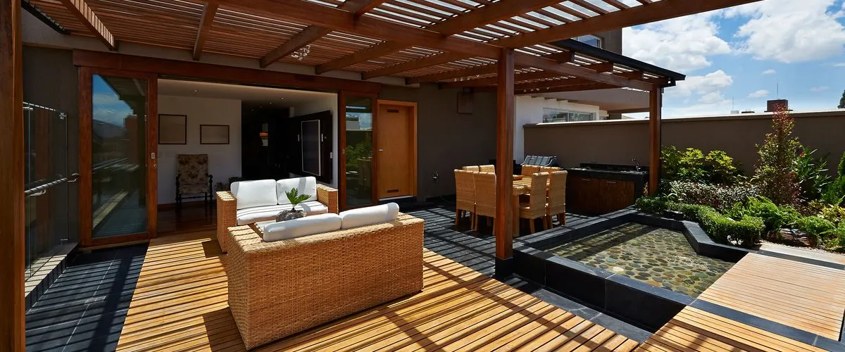 Modern outdoor patio with a wooden pergola, featuring white cushioned wicker-style armchairs, a matching sofa, and a coffee table
