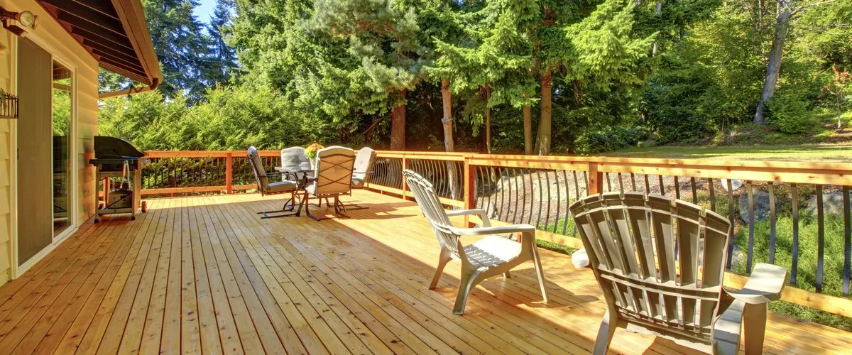 Spacious wooden deck attached to a house, featuring chairs, reclining patio chairs, and a barbecue grill near the wall