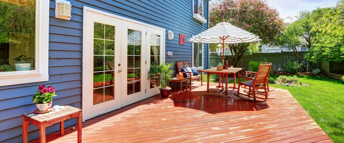 Backyard patio with red wooden decking attached to a blue house with white trim