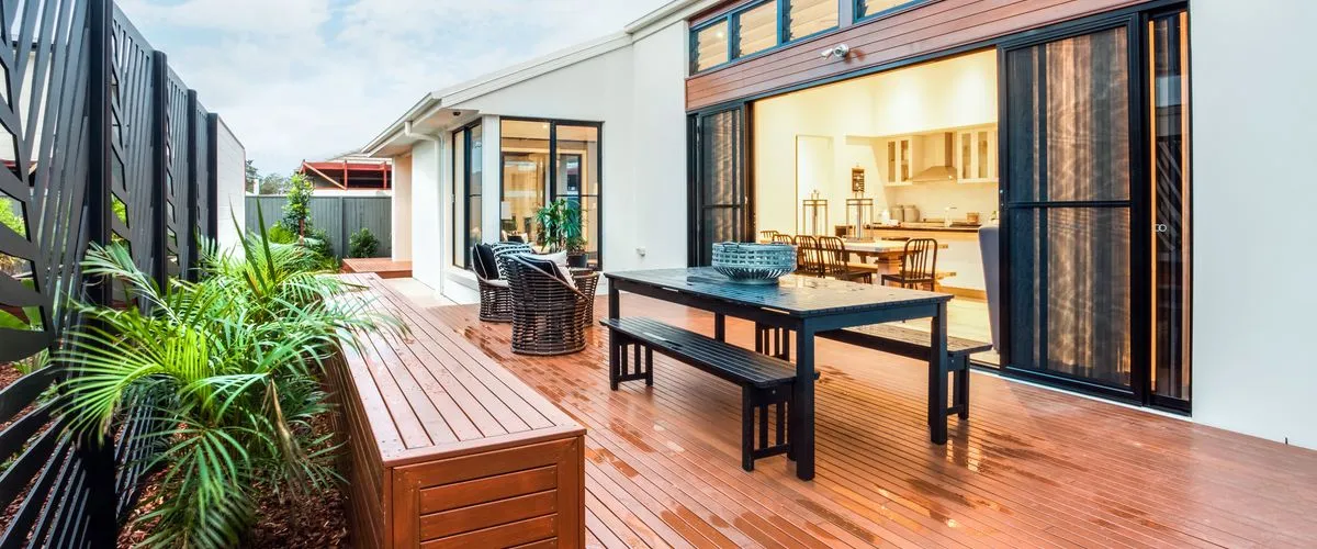 Modern outdoor patio with a wooden deck featuring a black dining table, matching benches, and wicker chairs