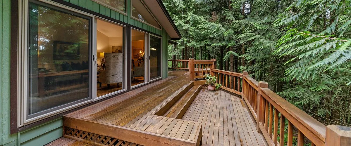 Elevated wooden deck attached to a forest-side home, featuring warm-toned planks, wooden railings, and steps leading to a lower level