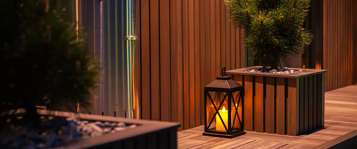 Evening outdoor scene featuring vertical wooden paneling and a deck with warm-toned planks.