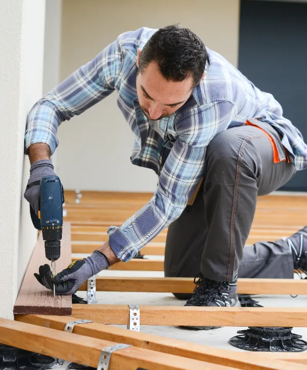 A man is installing wooden decking using adjustable pedestal feet