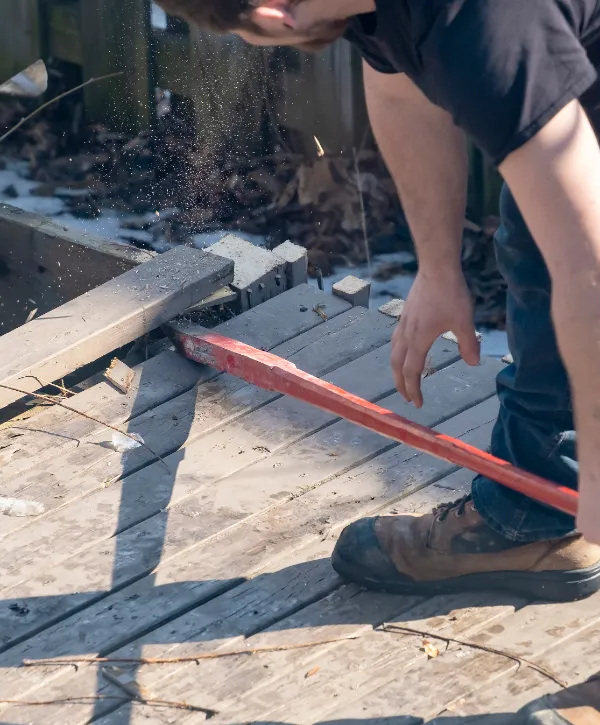 A person is using a pry bar to dismantle an old wooden deck